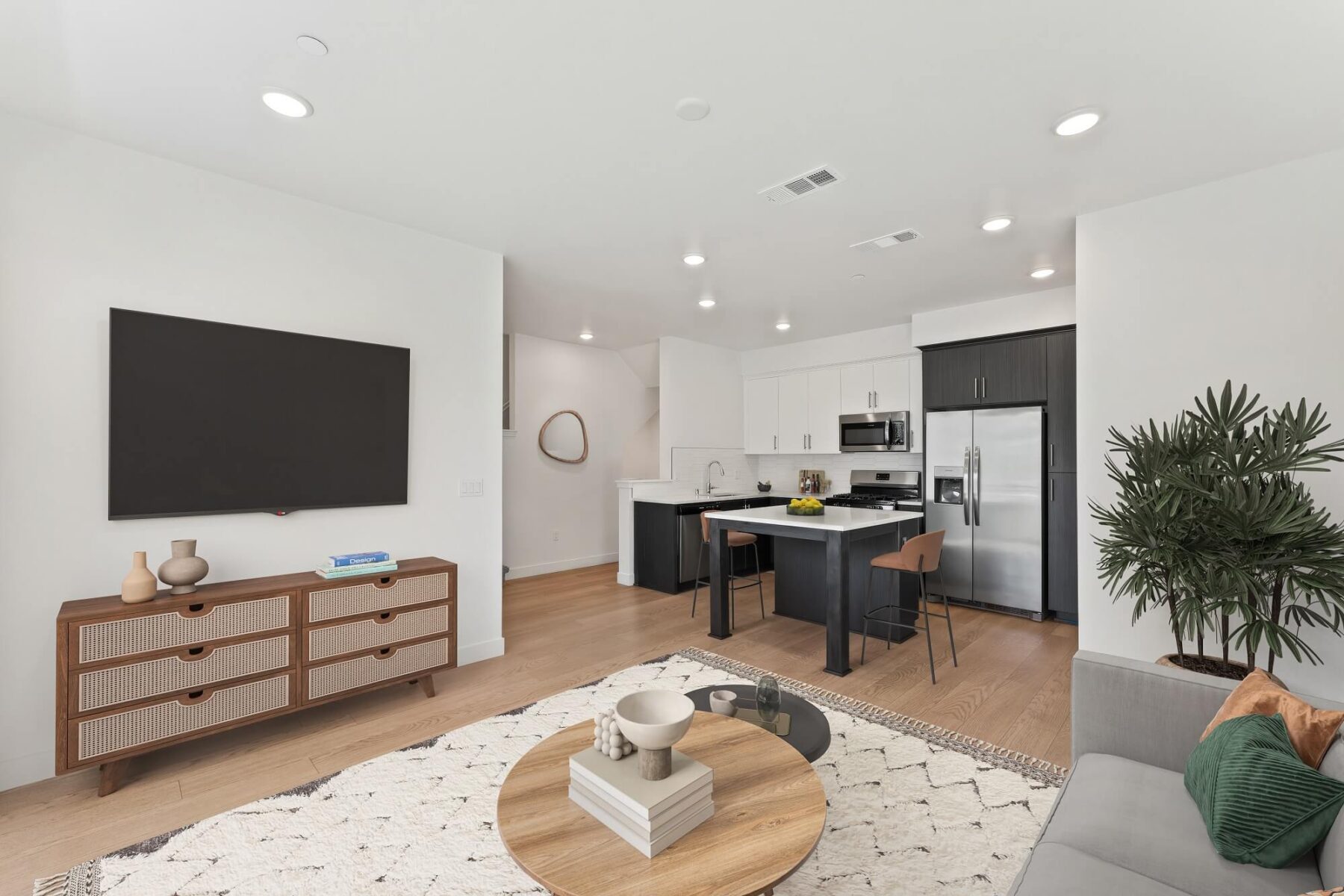 Living room with couch seating, wood-style flooring, television, designer lighting and open access to kitchen